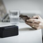 Person Holding Iphone Beside Black Portable Speaker